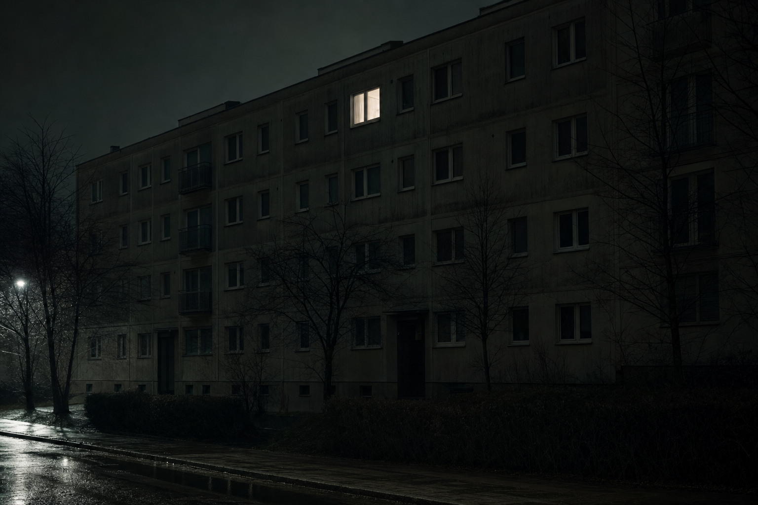 Blok nocą w deszczu, jedno zapalone okno po naprawie